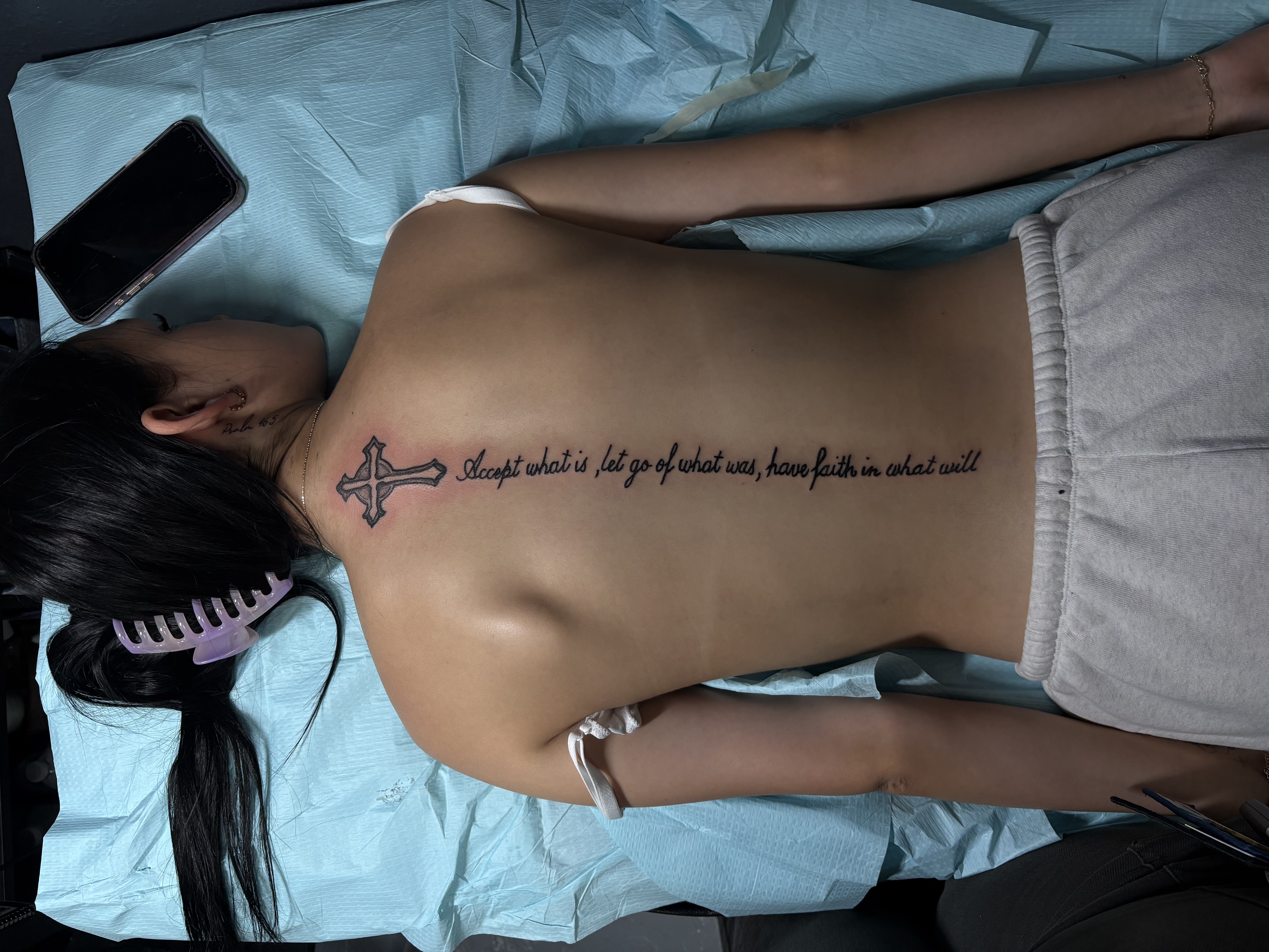 Freshly completed spine tattoo with a cross and script.