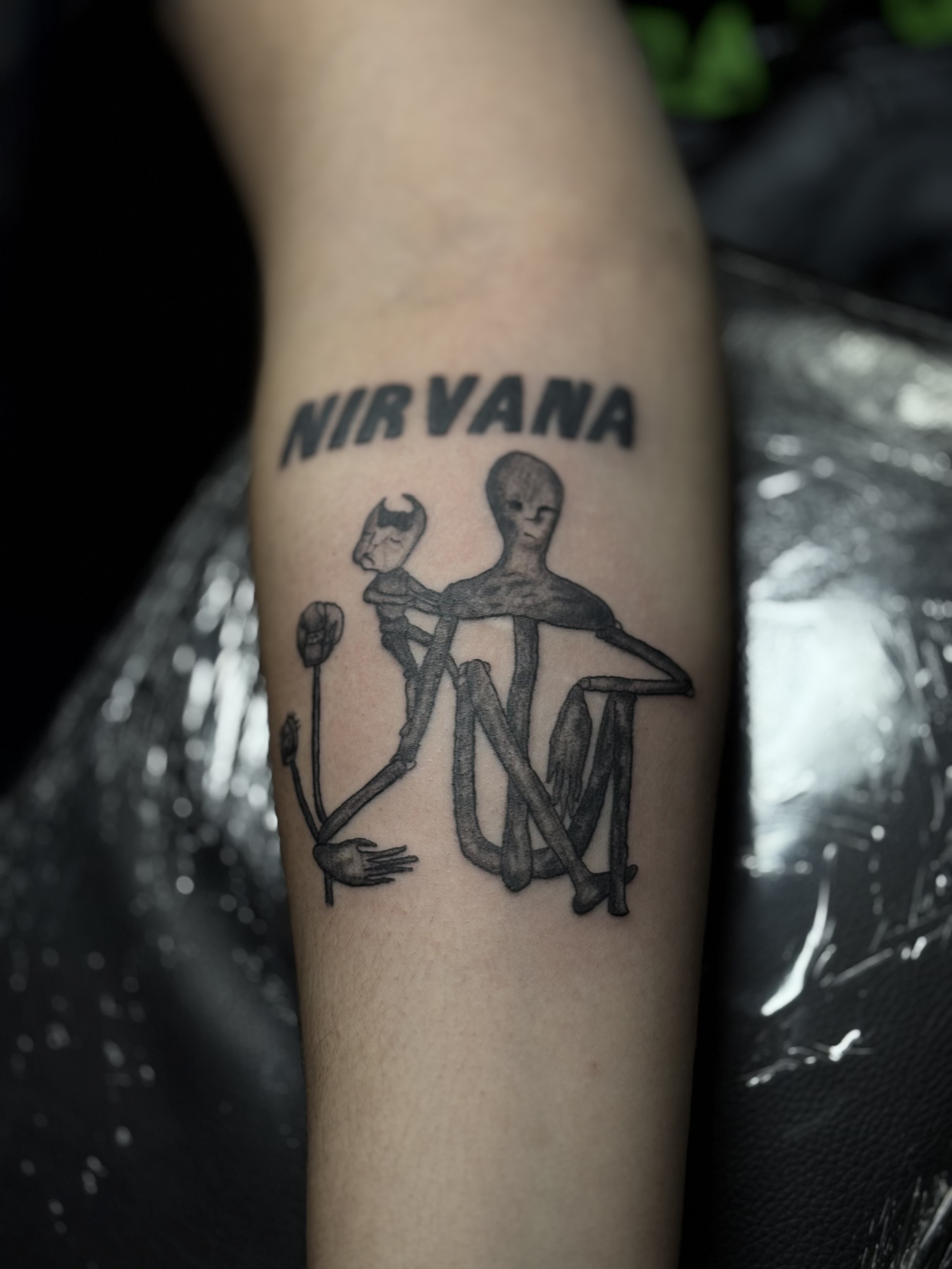 Forearm tattoo with the word NIRVANA and stylized figures.